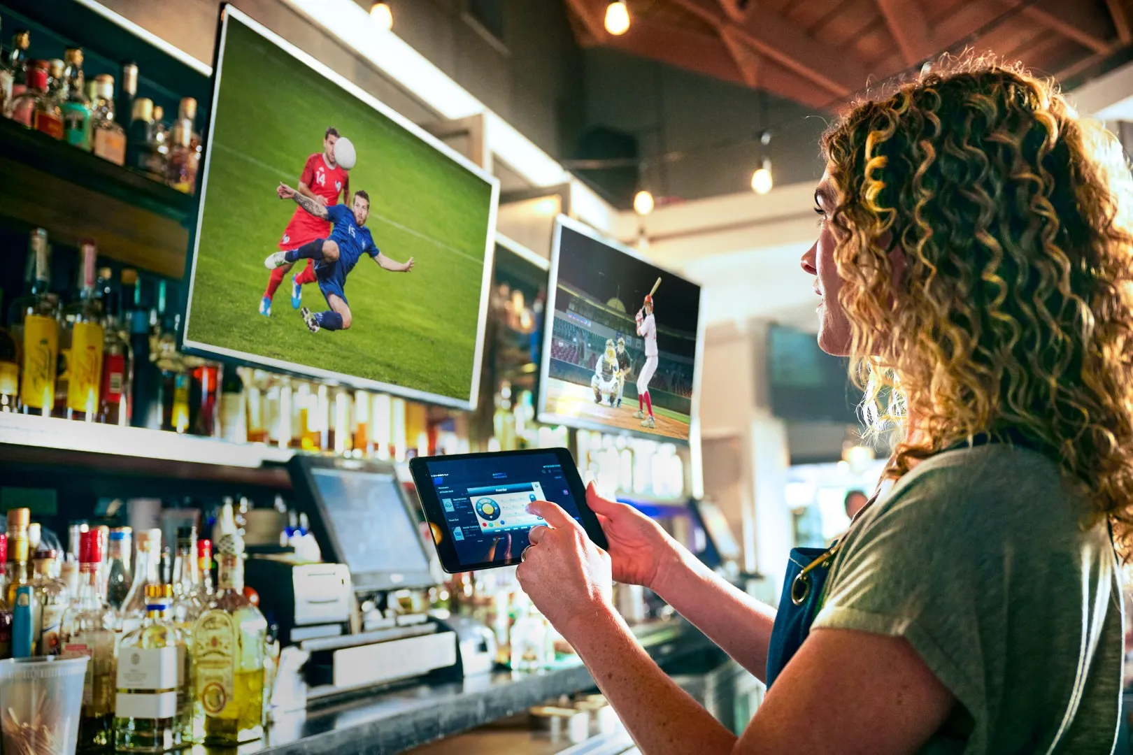 Bartender changing the game on a tablet in front of a wall of TVs