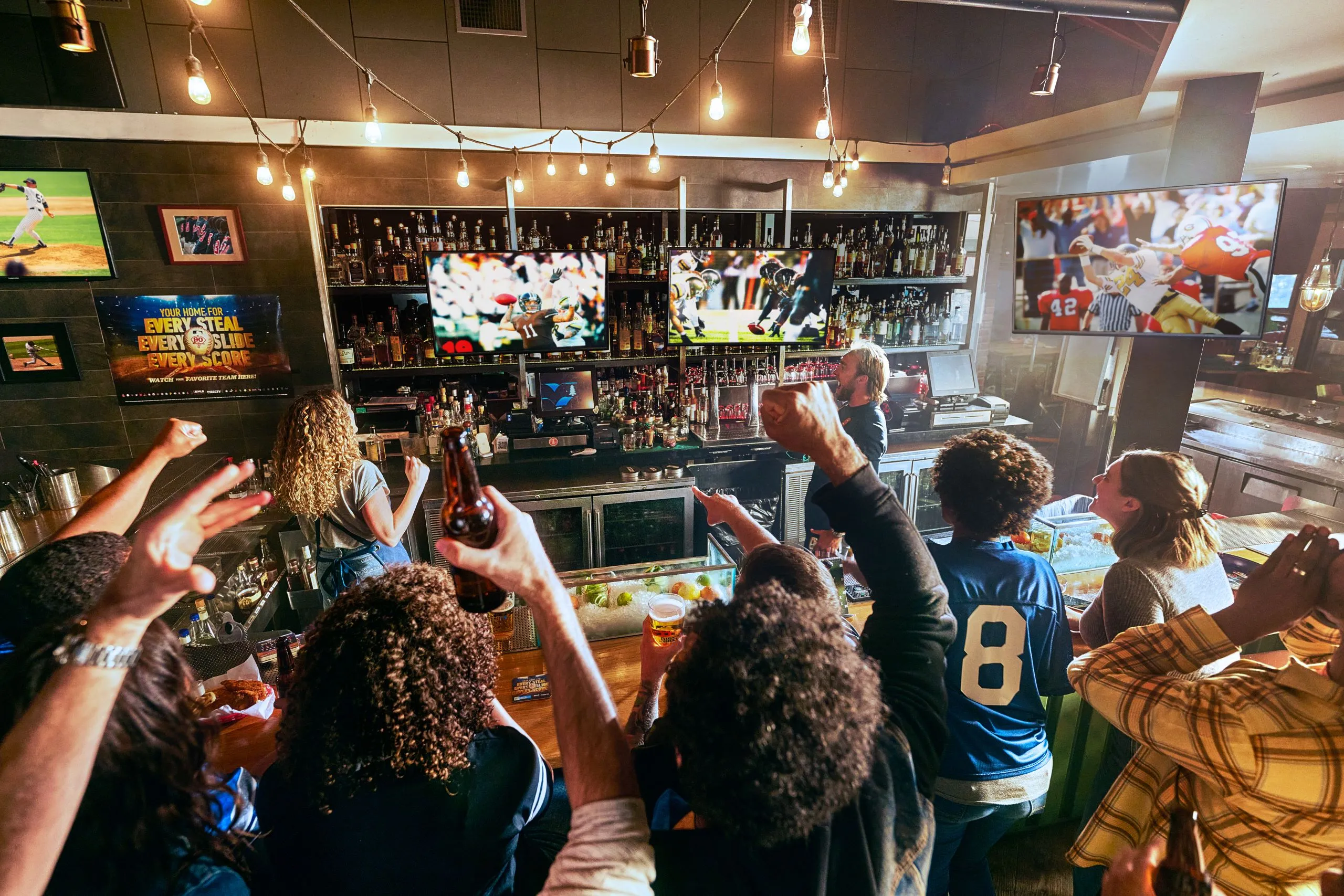 Fans cheering in a sports bar with DIRECTV on screens behind the bar